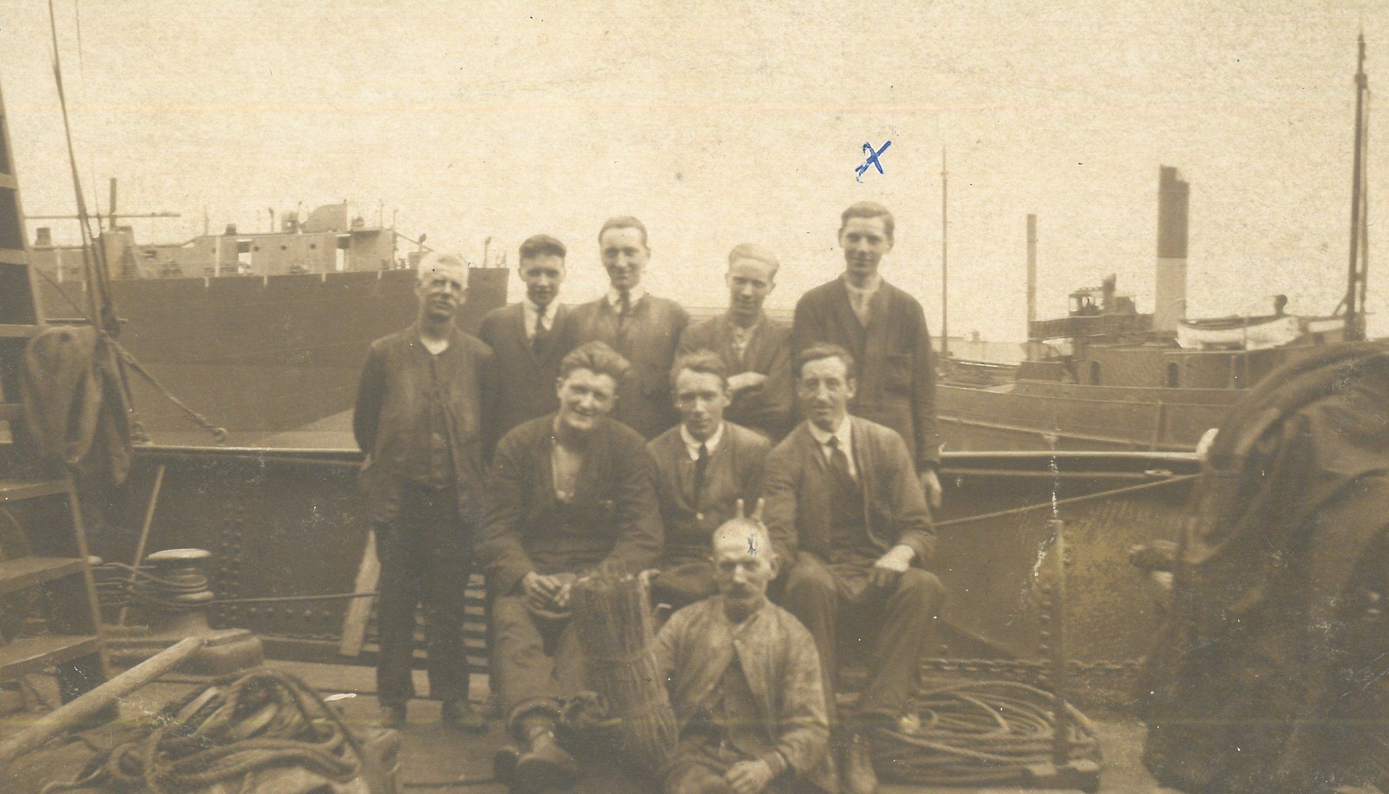 An old image of workers from the business many years ago smiling aboard one of the ships they have been working on. One of the workers has put his fingers up jokingly behind an older man.