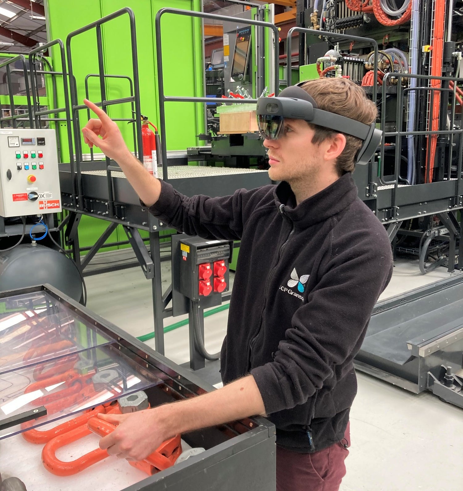 An employee at CCP Gransden working on the shop floor touches a virtual button as he carries out a production process step guided by a microsoft hololens augmented reality headset