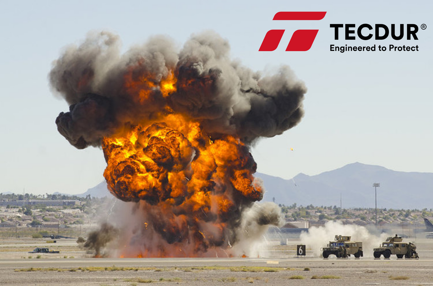 A photo of an explosion in an arid environment besie two armored vehicles. The Tecdur logo is overlayed beside this with the caption "Engineered to protect". Tecdur products are produced by CCP Gransden's sister company Hamilton Erskine