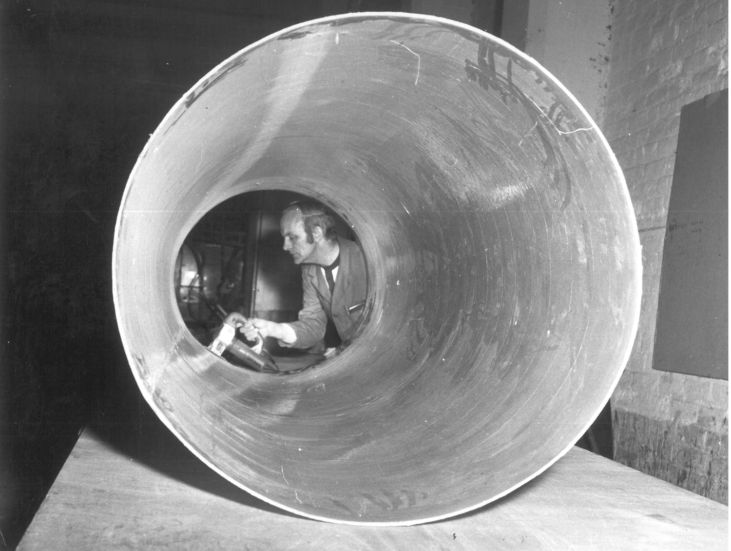 A black and white photograph shows an employee sanding the inside of a tank